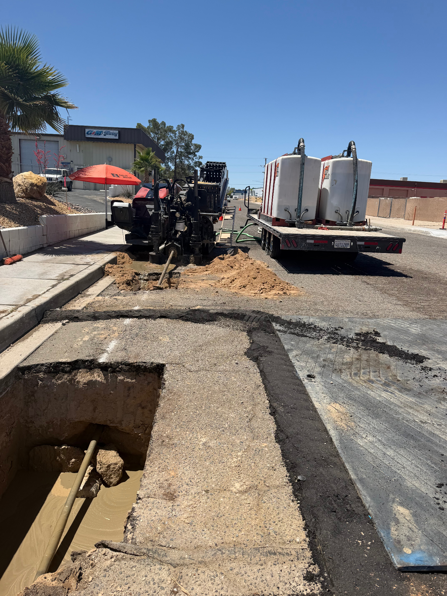 Ditch Witch rig boring alongside curb with vac tanks staged